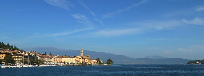 Trip Reisetipps beliebte Urlaubsziele am Gardasee -  Mit einer Fläche von 370 km² ist der Gardasee der größte See Italiens. Es liegt am Fuße der Alpen und erstreckt sich über drei Staaten: Lombardei, Venetien und Trentino. Die maximale Tiefe des Sees beträgt 346 m, er hat eine längliche Form und sein nördliches Ende ist sehr schmal. Dort ist der See von den Bergen der Gruppo di Baldo umgeben. Du trittst aus deinem gemütlichen Hotelzimmer und es begrüßt dich die warme italienische Sonne. Du blickst auf den atemberaubenden Gardasee, der in zahlreichen Blautönen schimmert - von tiefem Dunkelblau bis zu funkelndem Türkis. Majestätische Berge umgeben dich, während die Brise sanft deine Haut streichelt und der Duft von blühenden Zitronenbäumen deine Nase kitzelt. Du schlenderst die malerischen, engen Gassen entlang, vorbei an farbenfrohen, blumengeschmückten Häusern. Vereinzelt unterbricht das fröhliche Lachen der Einheimischen die friedvolle Stille. Du fühlst dich wie in einem Traum, der nicht enden will. Jeder Schritt führt dich zu neuen Entdeckungen und Abenteuern. Du probierst die köstliche italienische Küche mit ihren frischen Zutaten und verführerischen Aromen. Die Sonne geht langsam unter und taucht den Himmel in ein leuchtendes Orange-rot - ein spektakulärer Anblick.